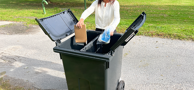 Kvinna håller i en kartongbit och en plastpåse över ett tvåfackskärl för fastighetsnära insamling